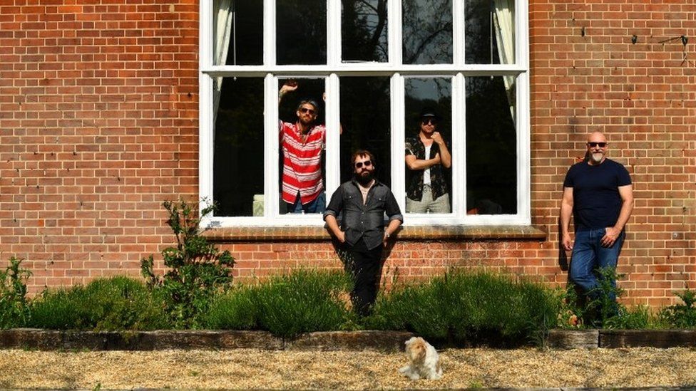 Band members pose in a garden as they isolate together with their families and pets in a rented luxury estate