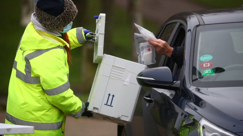 A worker collects a swab from a car window at a test centre in Goldsworth Park in Surrey