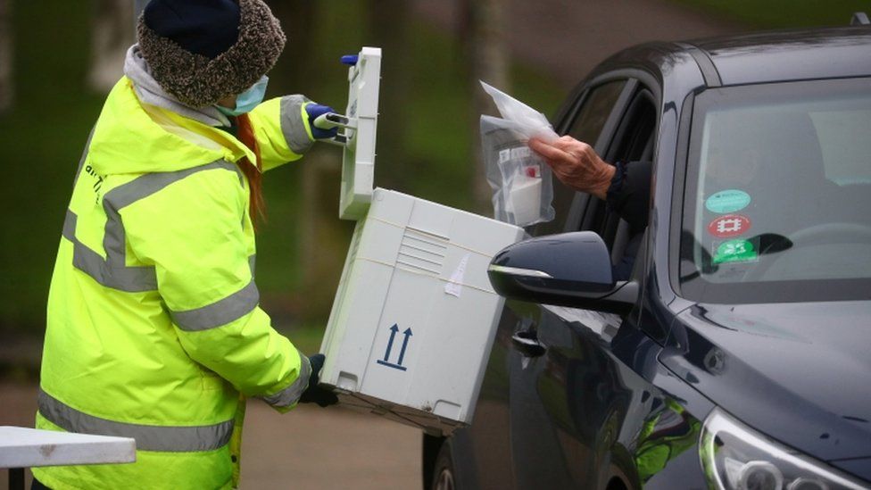 A worker collects a swab from a car window at a test centre