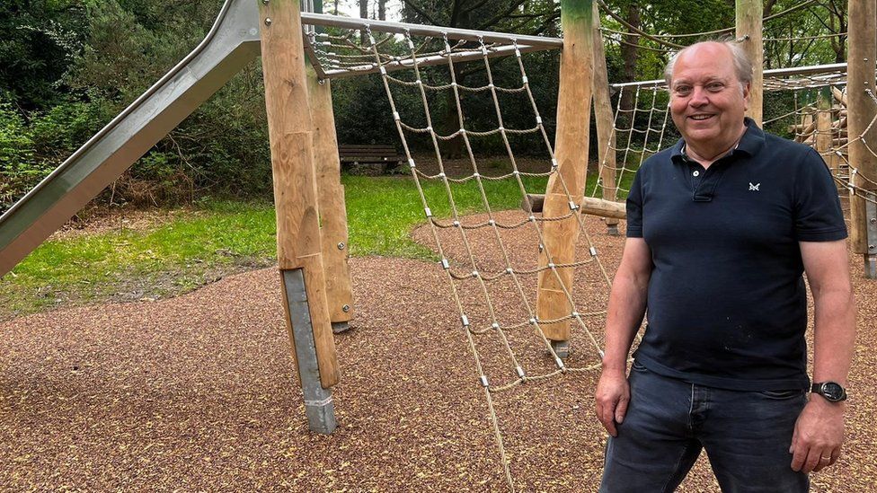 Colin Elkins standing in the new playground in front of a timber frame and metal slide