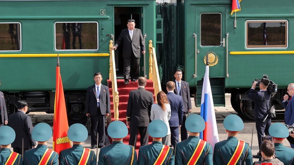 Kim Jong Un stands at the top of a staircase leading to his green train in front of an assembly of uniformed officials on 13/9