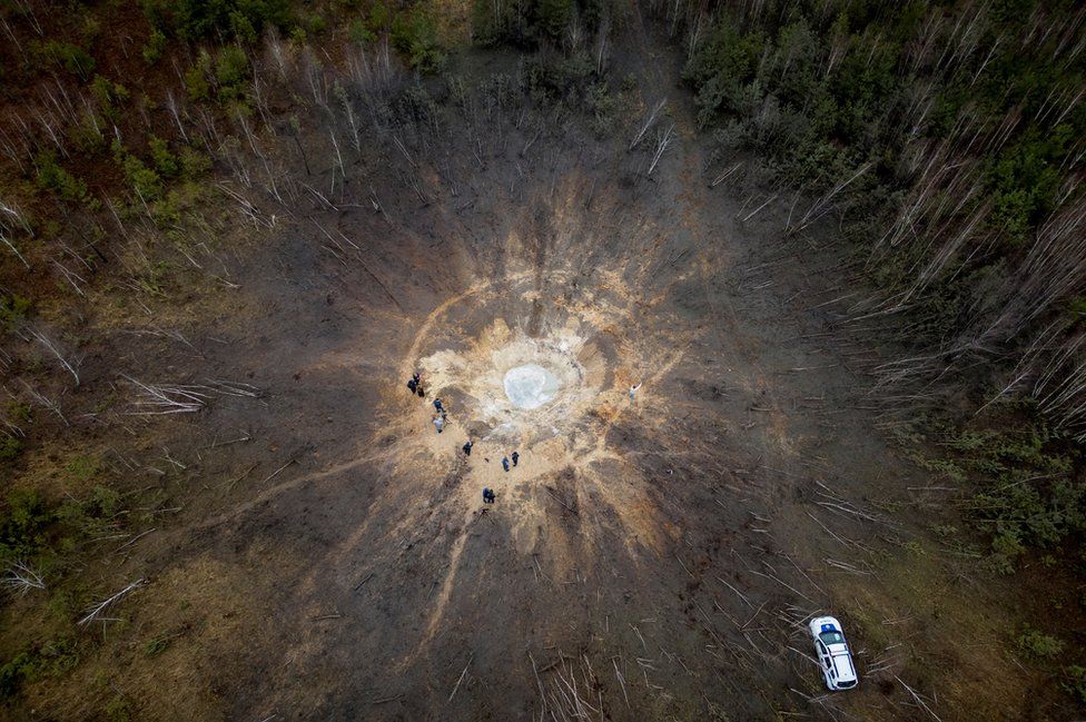 People stand around a crater made by a Russian missile strike in the village of Buda-Babynetska, outside Bucha, near Kyiv, Ukraine