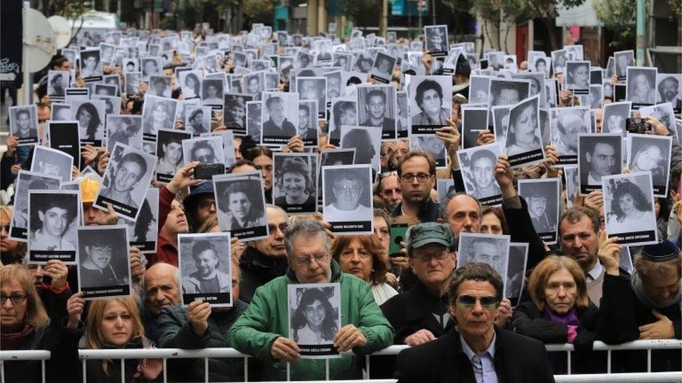 Picture released by Noticias Argentinas showing people holding pictures of victims of the 1994 bombing attack against the Argentine Israelite Mutual Association (AMIA) Jewish community center that killed 85 people and injured 300, during the commemoration of the attack's 25th anniversary, in Buenos Aires on July 18, 2019.