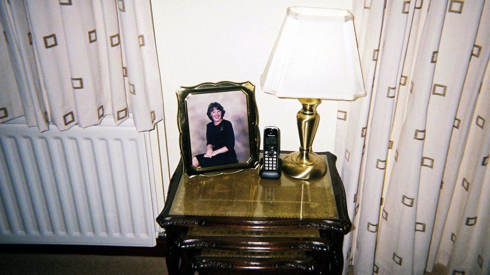 A telephone on a table beside a lamp and picture of a woman