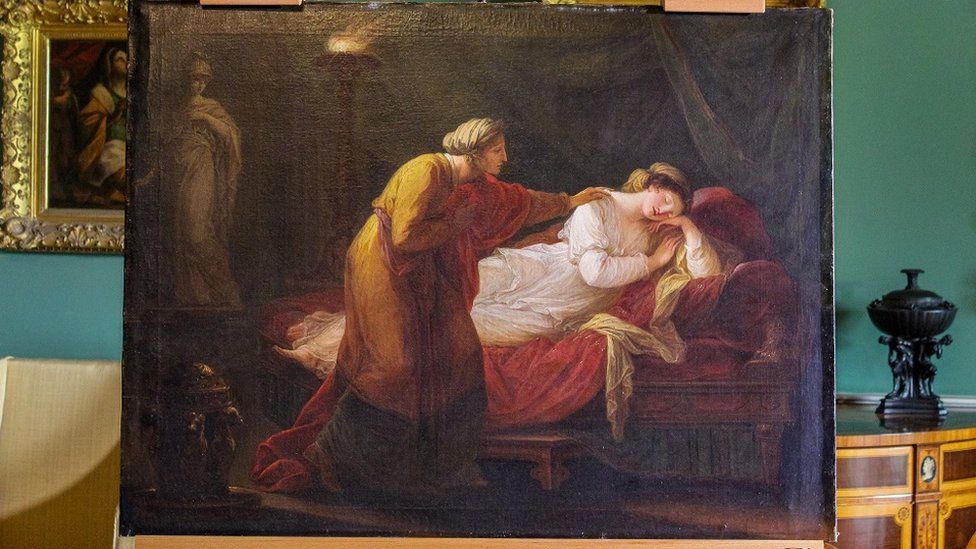 Oil painting of two women classically dressed in toga-like garments, one comforts the other. Painting sits unframed on an easel.