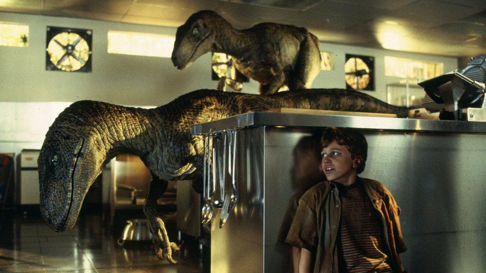 A scene from the film Jurassic Park - a young boy hides from two velociraptors in a kitchen