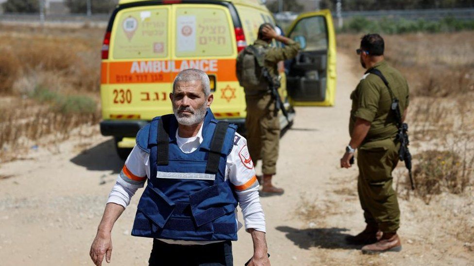 An Israeli medic walks near soldiers and an ambulance after the attack on the Kerem Shalom crossing, near Israel's border with Gaza in southern Israel, 5 May 2024.