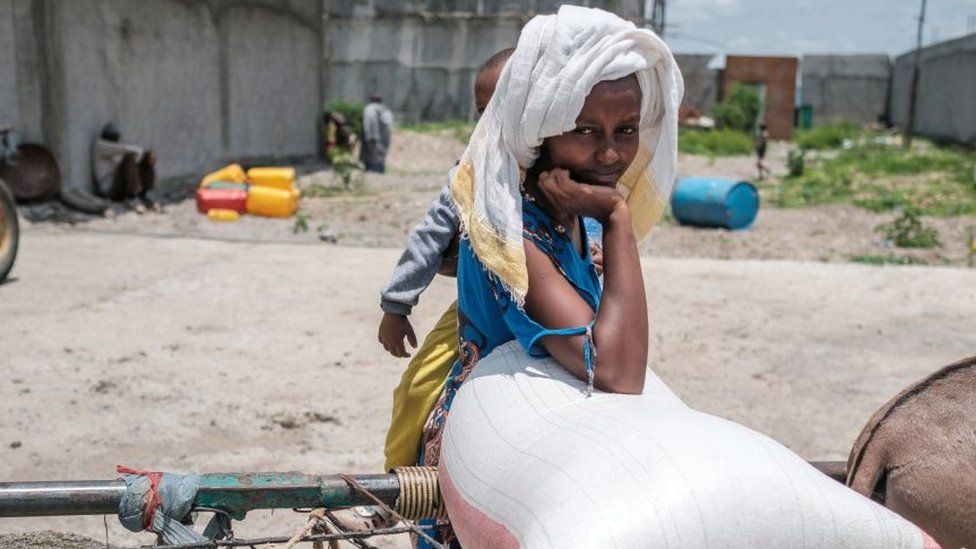 A woman holds a baby as she rests over a sack of wheat during a food distribution