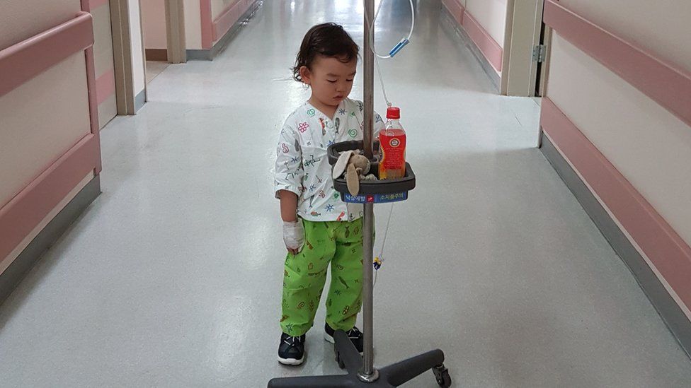 Small boy with wheeled drip stand in a hospital corridor