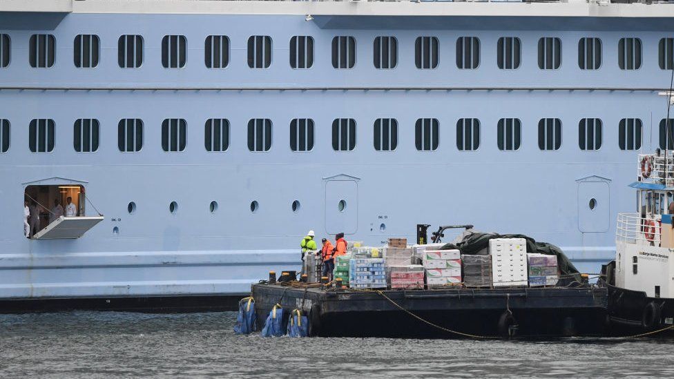 hatch opened on side of cruise ship with supply tug alongside