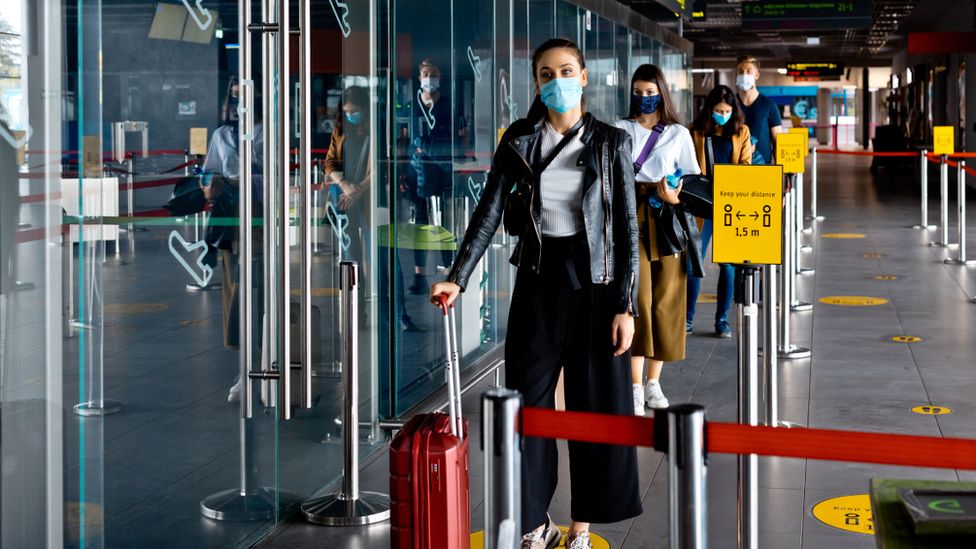 Путешественники в масках стоят в очереди в аэропорту