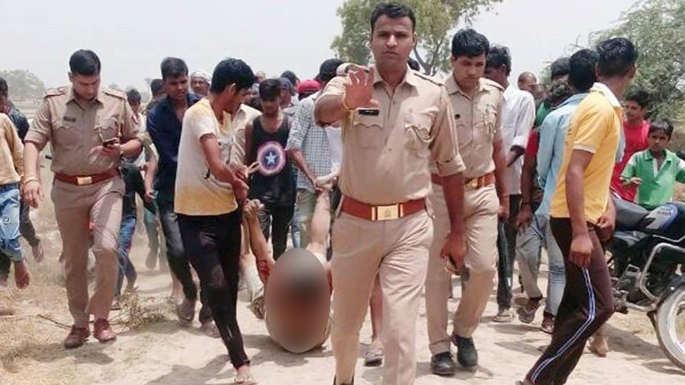 A picture of a victim of lynching being dragged in front of a group of policemen.