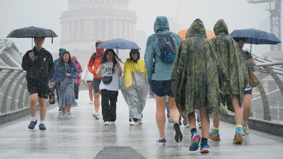 People caught in heavy rain while crossing the Millennium Bridge in central London on 2 August