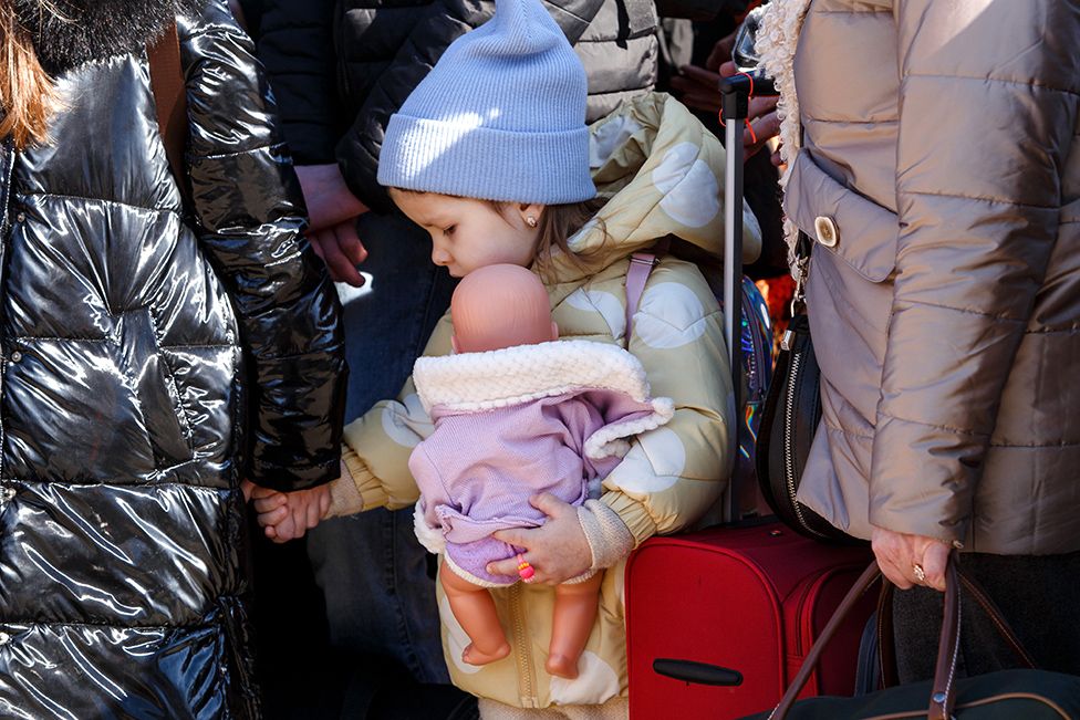 A little girl holding a woman's hand clutches a doll at the Uzhhorod-Vysne Nemecke checkpoint on the Ukraine-Slovakia border