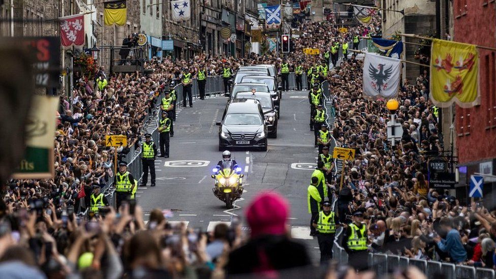 Members of the public gather on the Royal Mile in Edinburgh to watch the hearse carrying the coffin of Queen Elizabeth II passes by