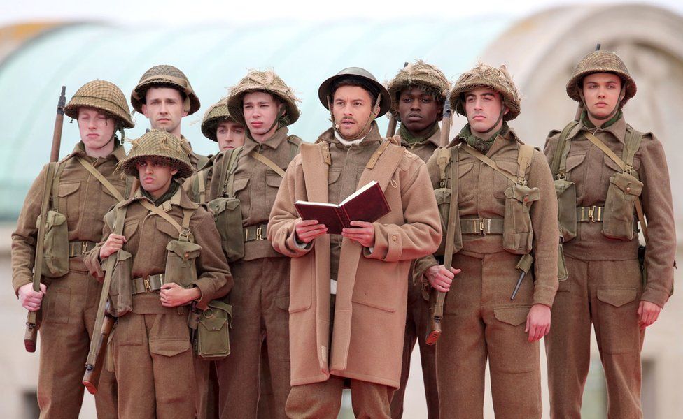 An actor dressed as a soldier reads from a book