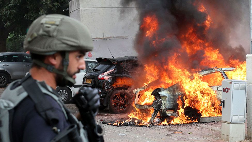 A member of the Israeli security forces stands close to a car hit by a rocket fired from Gaza, in the southern Israeli city of Sderot, on 9 October 2023