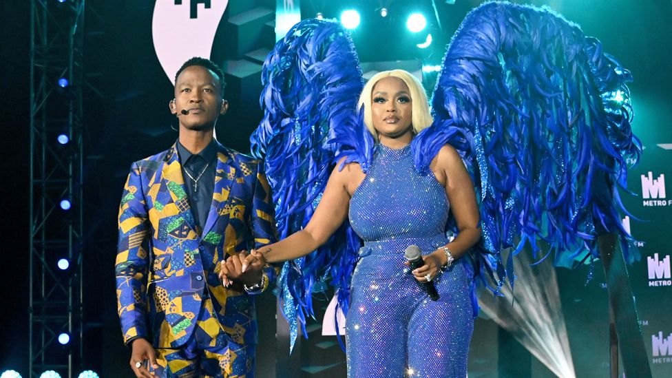 South Africa presenters Katlego Maboe (in a yellow and blue suit) and Lerato Kganyago on stage at Mbombela Stadium, South Africa - Saturday 6 May 2023