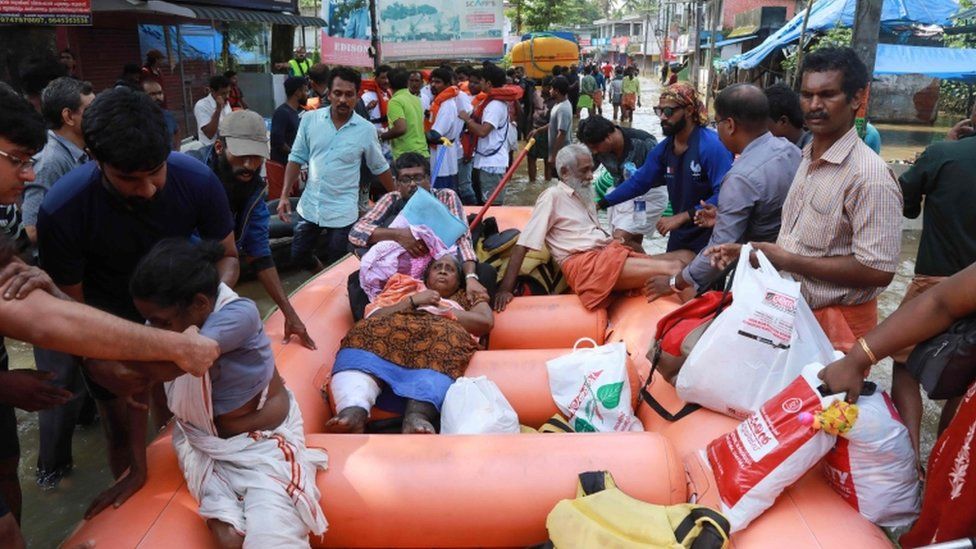 Indian men and women are evacuated by rescue workers using an orange rescue dinghy