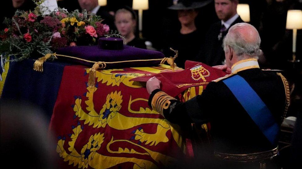 King Charles III places the the Queen's Company Camp Colour of the Grenadier Guards on the coffin