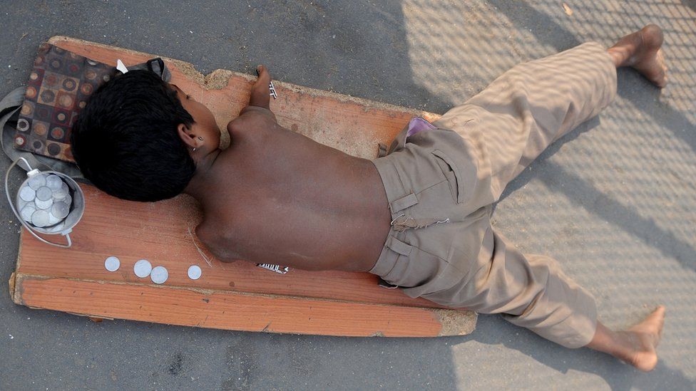 File photo: A handicapped child lies on a mat while begging for alms next to a few Indian rupee and paise coins given to him in Mumbai on December 7, 2011