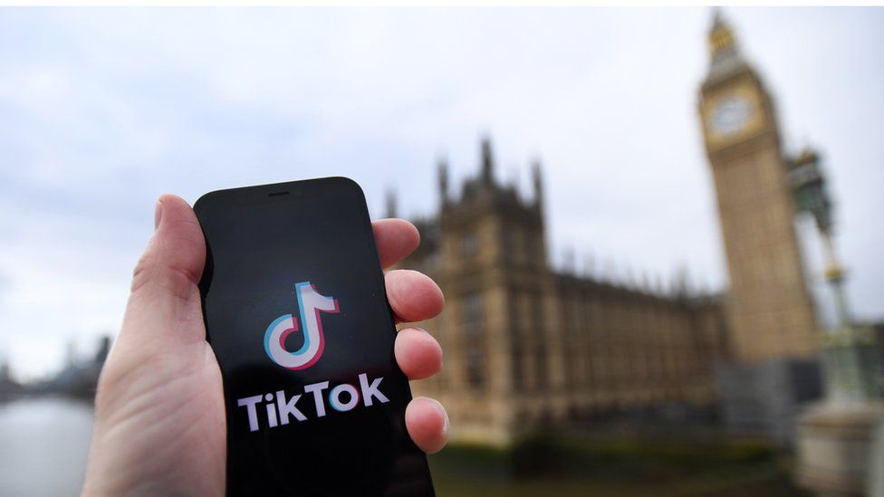 Person holding a device with the Tiktok logo outside Parliament