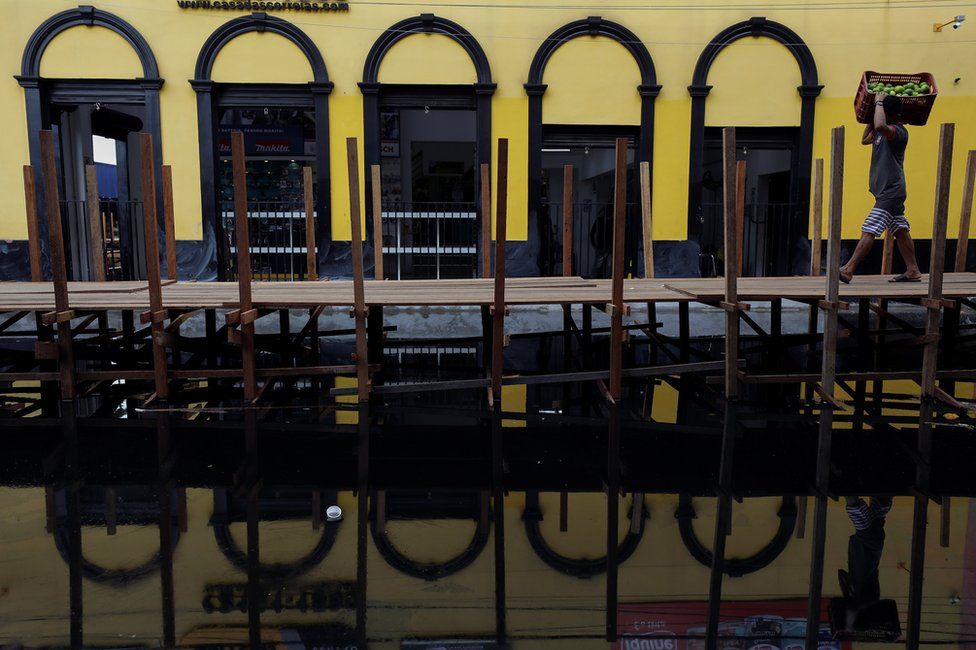 A man carries a box with oranges as he walks over wooden walkways installed by the city hall over a street flooded by waters from the Negro river in Manaus