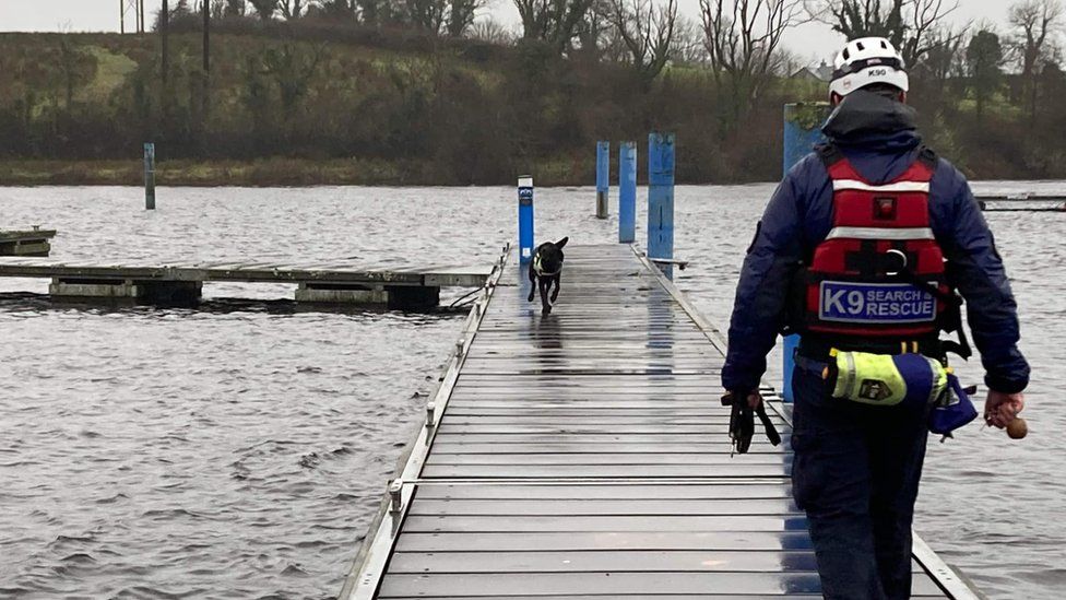 A sniffer dog and their handler search for a missing person at a lake