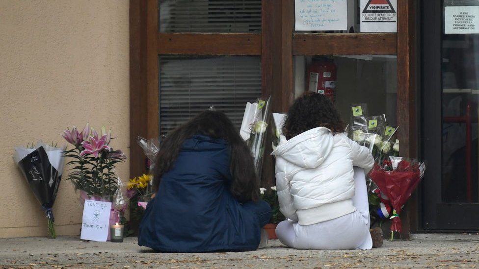 Youngsters look at floral tributes laid at the school in Conflans Saint-Honorine where the murdered teacher was from, on 17 October 2020
