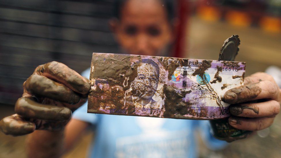 A Filipino resident displays money recovered amongst salvageable materials