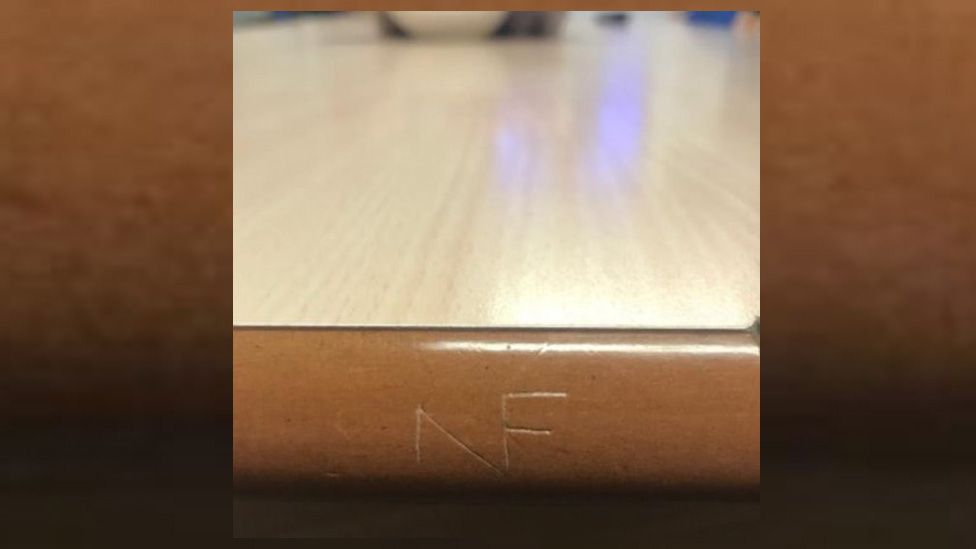 NF logo scratched on to the side of a table