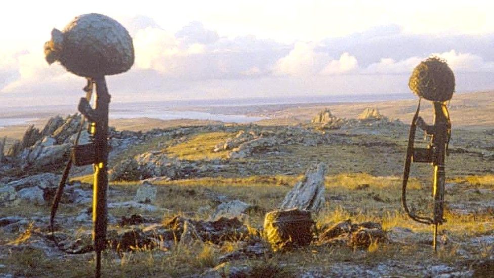 Helmets mounted on guns stuck into the ground on Mount Longdon, Falklands