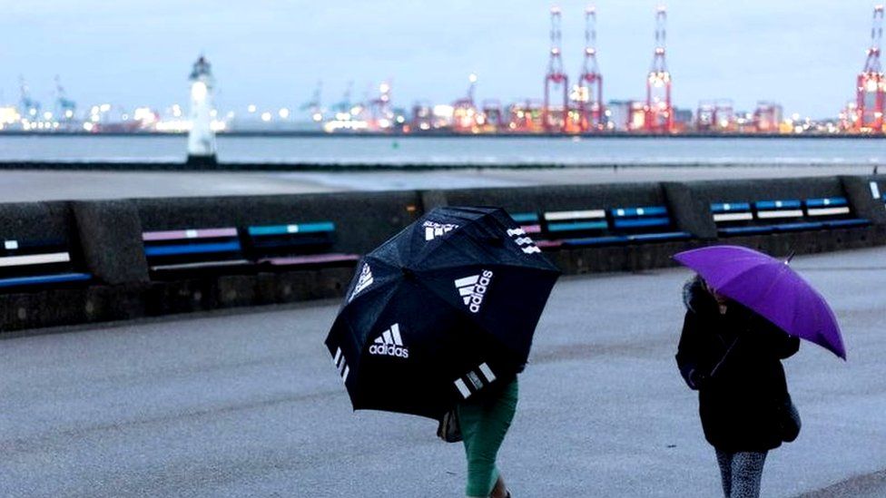 Two people walk along New Brighton promenade holding umbrellas