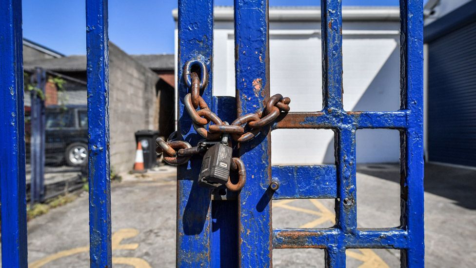 File image of a rusty chain and padlock securing blue painted steel gates to prevent access to a business on a trading estate in Bristol