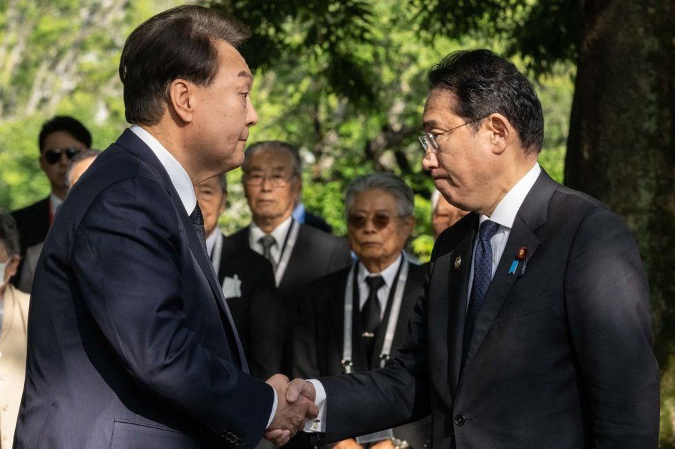 Юн Сук Ёль из Южной Кореи (слева) и премьер-министр Японии Фумио Кисида обмениваются рукопожатием во время посещения «Памятника корейским жертвам атомной бомбы» возле Мемориала в Парке мира во время встречи лидеров саммита G7 21 мая. 2023 г. в Хиросиме, Япония