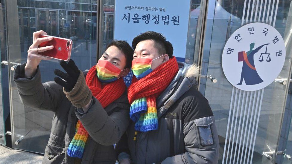 A pair wearing rainbow scarves and masks take a selfie outside a court house in South Korea in 2022