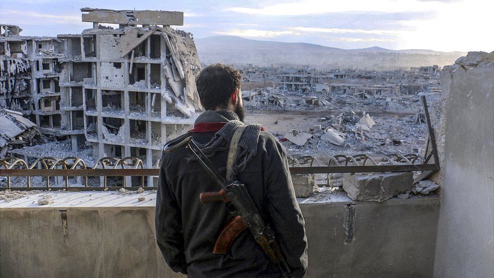 A Syrian stands guard as wreckage of collapsed buildings are seen at Darayya town, Syria, 28 January 2016