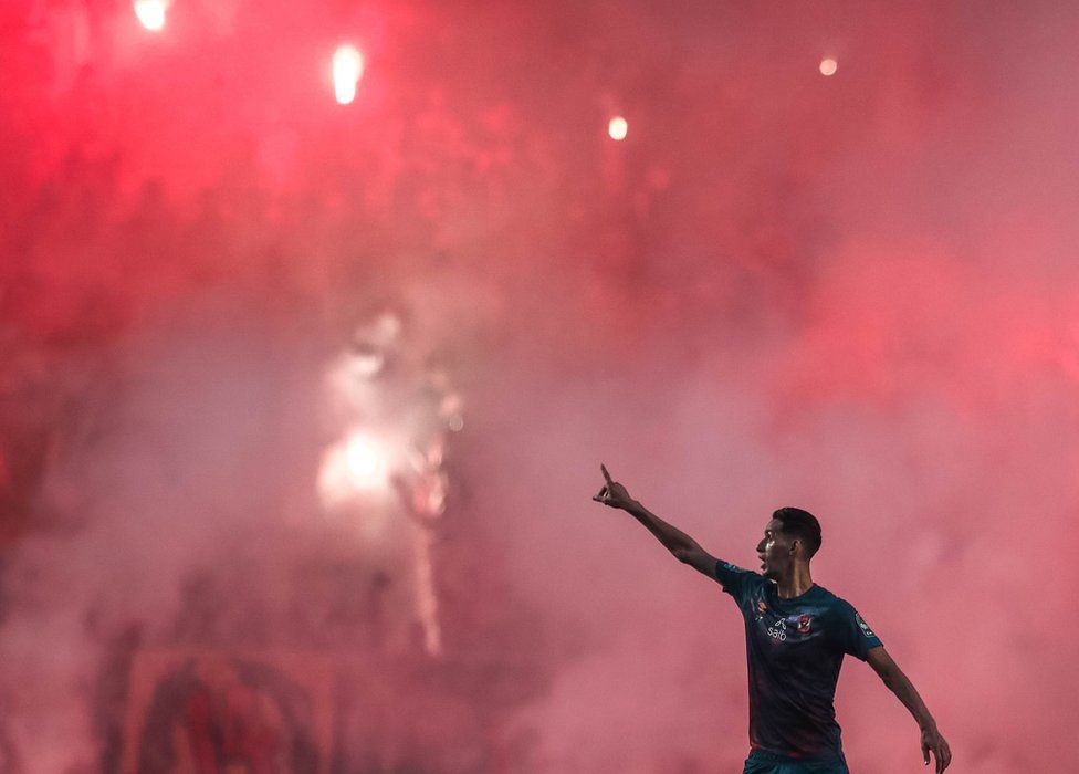 A footballer in front of a red mist in the Olympic Stadium in Rades, Tunisia - Saturday 19 June 2021