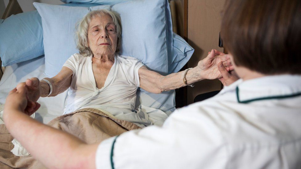 A woman lying in bed holding the hands of a carer