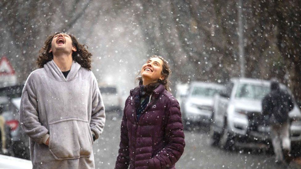John Henning (L) and Christina Steyn (R) enjoy the rare sight of snow falling in Johannesburg as a cold front sweeps across the country bringing sub-zero temperatures in Johannesburg on 10 July.