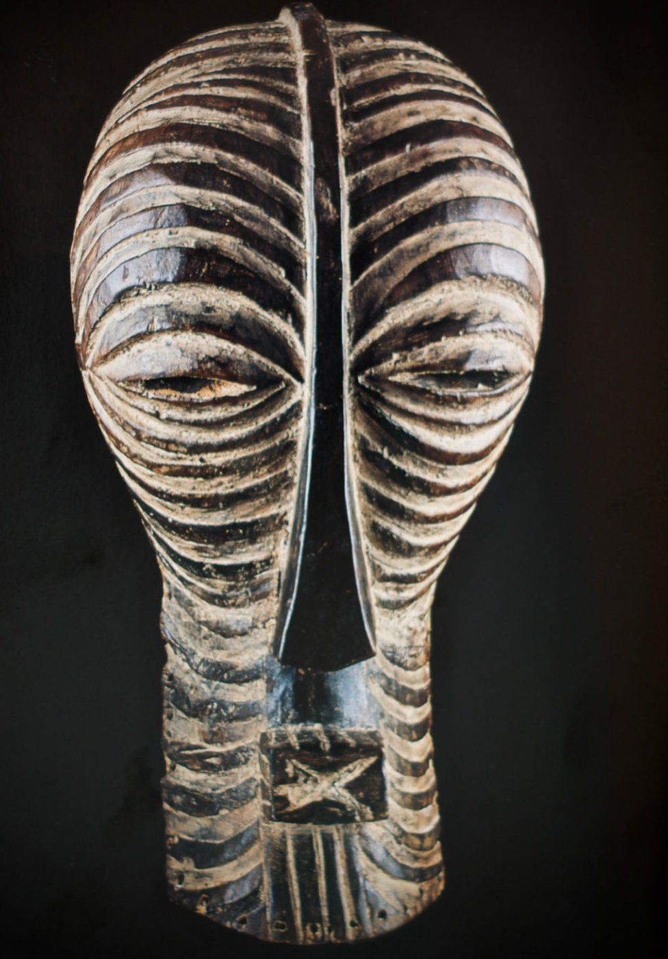 A carved wooded mask depicting an elongated face