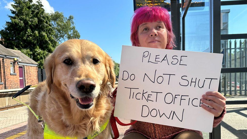 Sarah Leadbetter holding a 'Please do not shut ticket offices down' sign alongside her guide dog, Nellie
