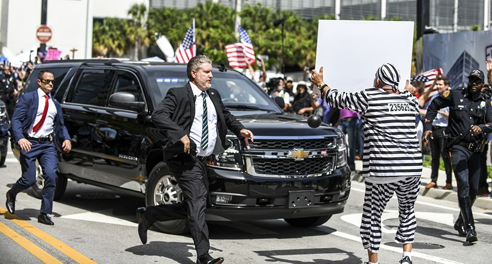 A protester runs out in front of former President Donald Trump's motorcade as it departs the Wilkie D. Ferguson United States Courthouse