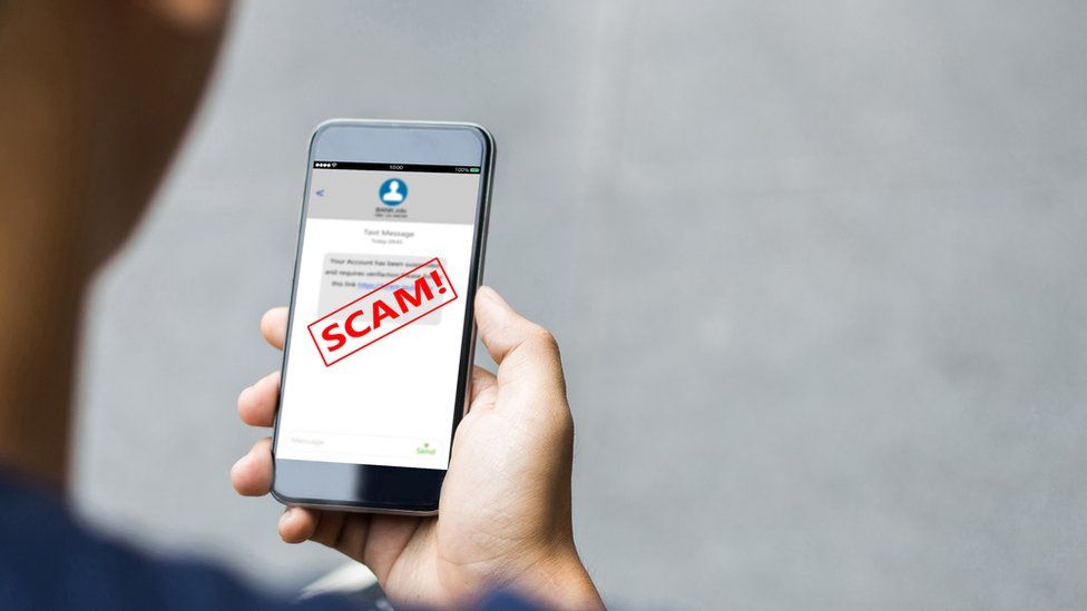 Picture of a hand holding a phone with a scam sign on it