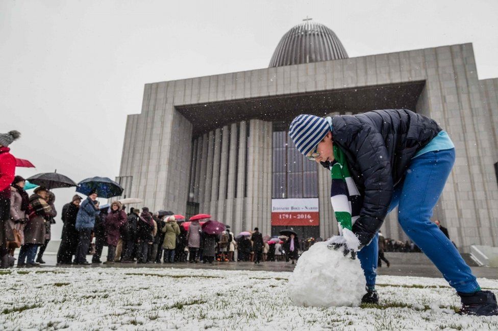 A young man makes a snowball as people queue to enter the Temple of Divine Providence before the opening ceremonies, on November 11, 2016.