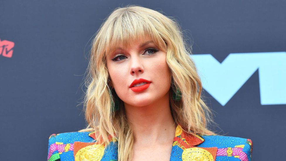 Taylor Swift head and shoulders, wearing a colourful jacket