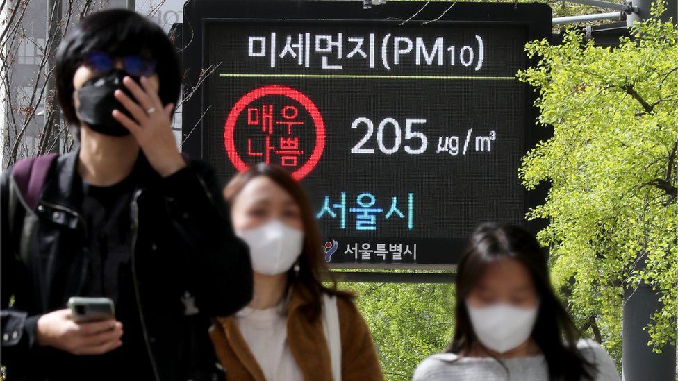 People wearing face masks walk in front of a health warning on yellow dust in Seoul.