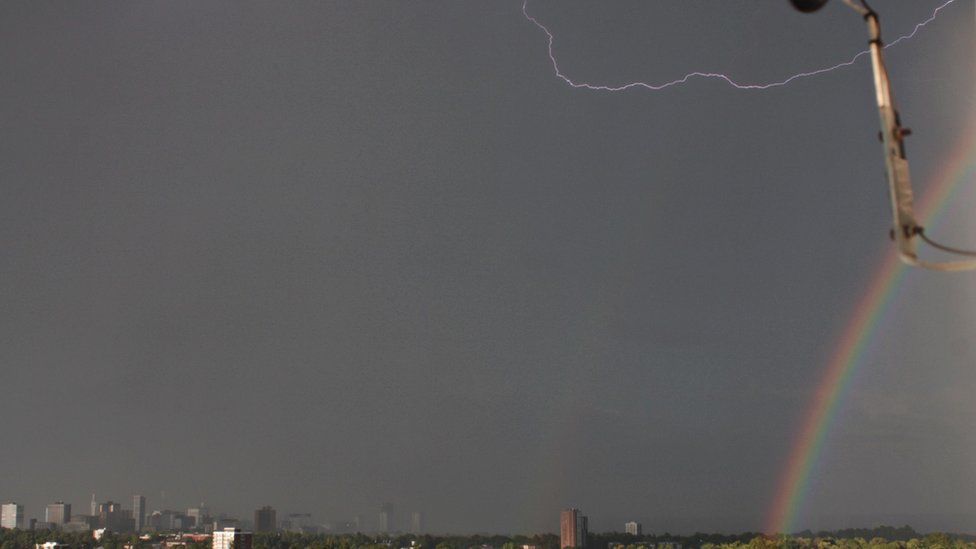 Rainbow and lightning strike over a city