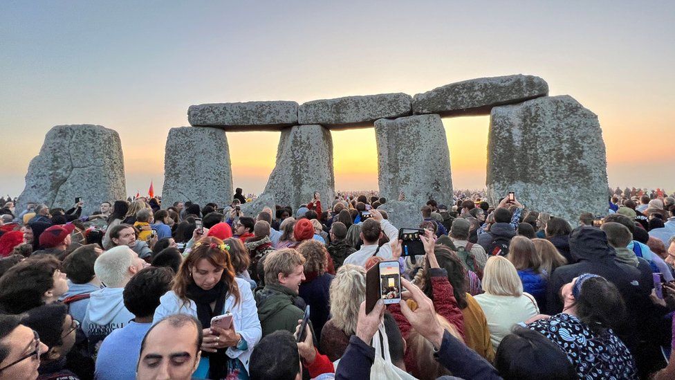 Crowds in front of Stonehenge as sun rises - people are taking photos with their phones