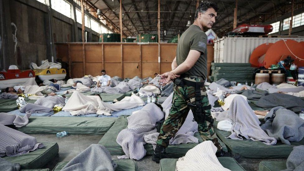 A member of the Coastguard overlooks survivors as they rest in a warehouse used as a temporary shelter, after a boat carrying dozens of migrants sank in the Ionian Sea, in Kalamata town, Greece, on June 14, 2023.